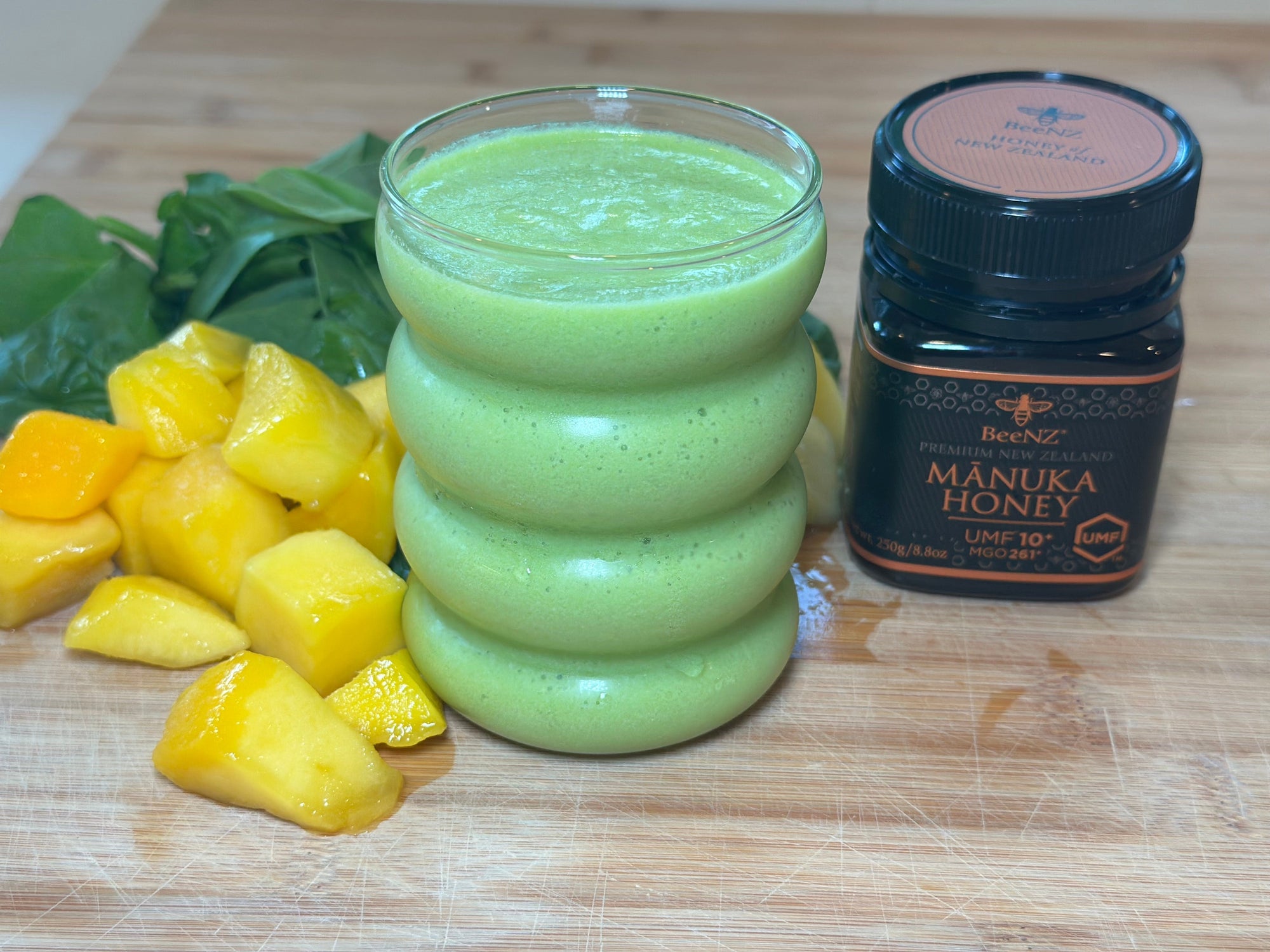 A creamy green smoothie in a glass, made with spinach, pineapple, mango, milk, and BeeNZ Manuka honey, representing a nourishing and easy back-to-school breakfast option for busy mornings.